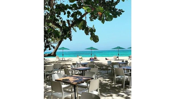 Espace extérieur aménagé avec des tables et des chaises, des parasols et une vue sur la plage et l’océan.