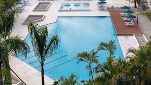 Une grande piscine avec plusieurs couloirs de nage, entourée de palmiers et de chaises longues.
