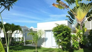 Un bâtiment moderne à l’extérieur blanc, entouré d’une végétation luxuriante et de palmiers.