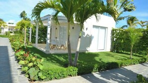 Un petit bâtiment blanc doté d’un espace extérieur abrité, entouré d’une végétation luxuriante et de palmiers.