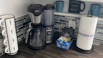 Una cocina con una cafetera, un hervidor y una taza de café sobre la encimera.