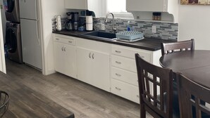 A compact kitchen with white cabinets, a black countertop, and a wooden dining table with chairs. - Comfy Bungalow (Lone Pine)