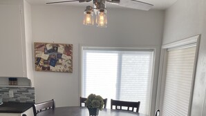 A dining area with a round table, six chairs, a ceiling fan, and a window with blinds. - Comfy Bungalow (Lone Pine)