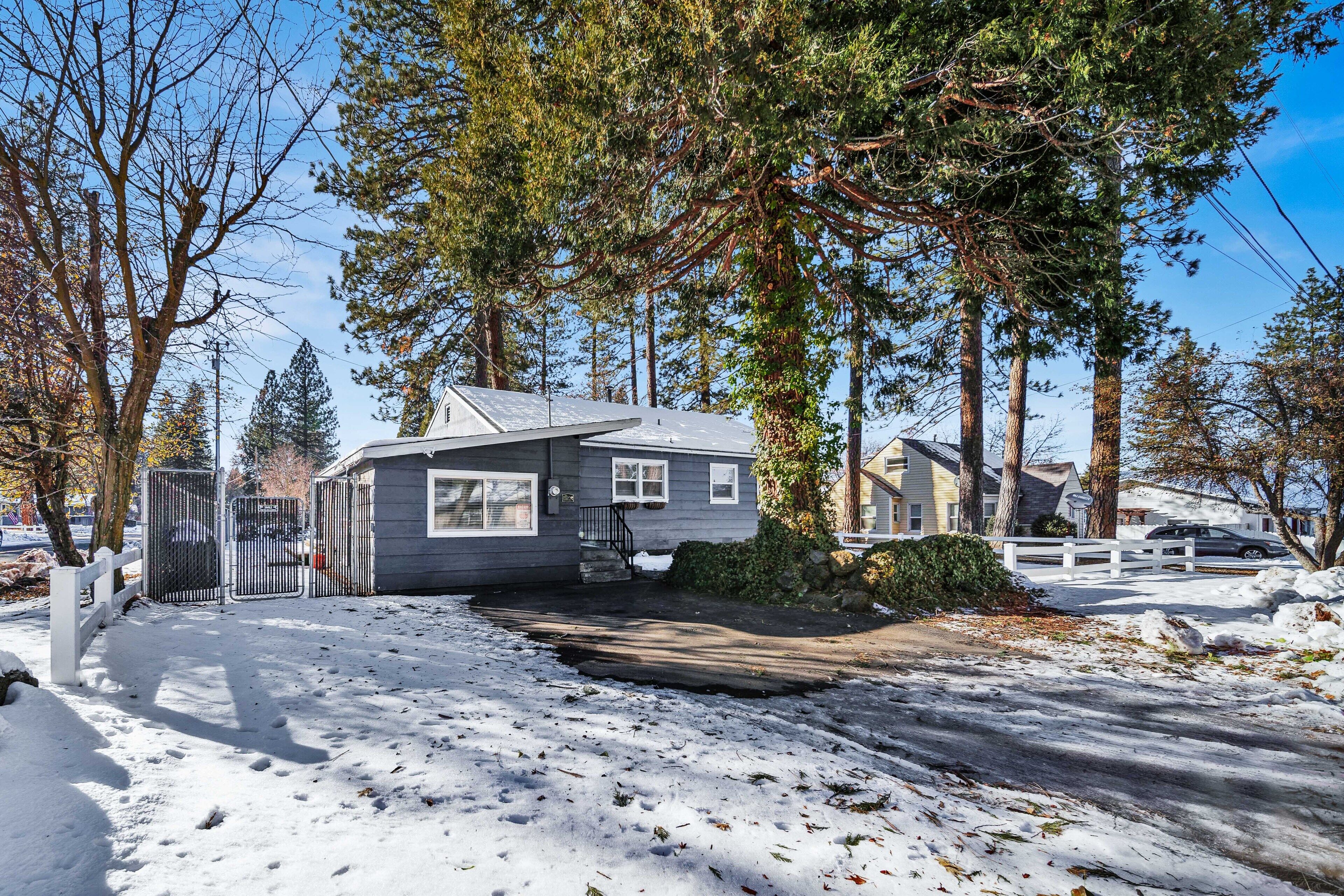 Une maison d’habitation avec une allée couverte, entourée de grands arbres et d’une cour enneigée.