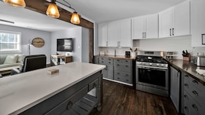 Een moderne keuken met witte kasten, een centraal eiland, een inbouwoven en hanglampen.