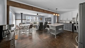 Een moderne keuken met een centraal eiland, houten balken, witte kasten en roestvrijstalen apparatuur.