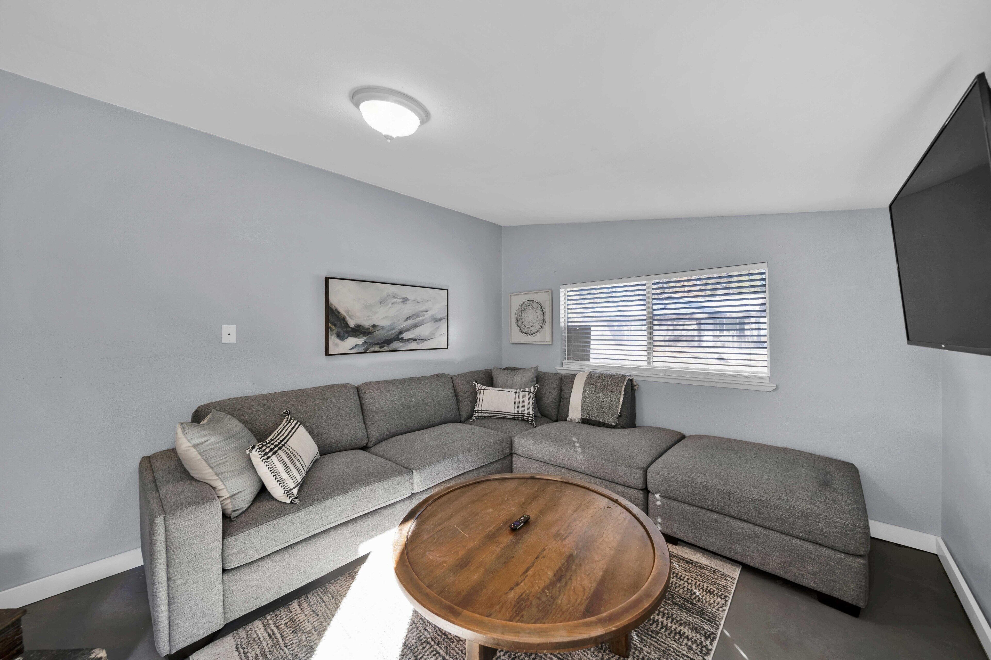 A modern living room with a sectional sofa, a round coffee table, and a flat-screen TV mounted on the wall.