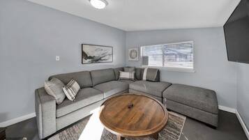 A modern living room with a sectional sofa, a round coffee table, and a flat-screen TV mounted on the wall.