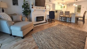 Ein Wohnzimmer mit einer Couch, einem Kamin, einem Fernseher und einem Essbereich mit Stühlen.