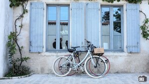 Un vélo est garé devant un immeuble aux volets bleus, et un panier est fixé au vélo.