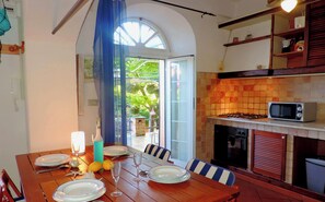 A dining area with a wooden table set for entry and dinner, a kitchen with a tiled backsplash, and a view through a glass door to an outdoor area.
