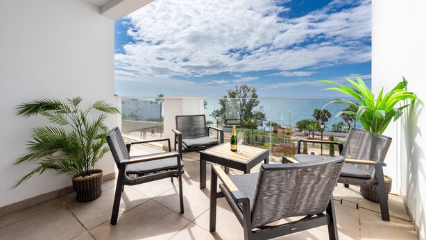 A balcony with wicker furniture, a bottle of champagne, and a view of the sea.