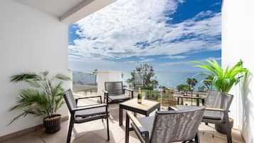 Een balkon met rieten meubilair, een fles champagne en uitzicht op zee.