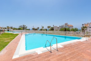 A swimming pool with a tiled deck, surrounded by a fence and palm trees.