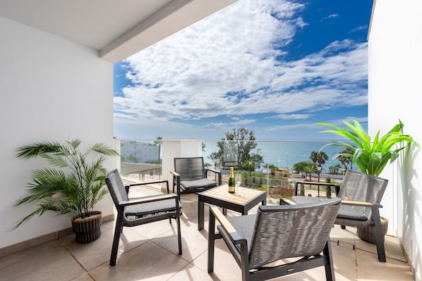 A balcony with outdoor furniture, a bottle of champagne, and a view of the sea.