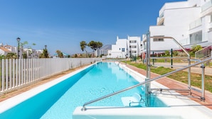 A swimming pool with a white fence, a metal ladder, and a clear blue sky.