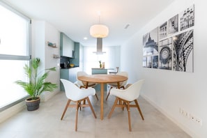 A modern kitchen with a dining area, featuring a round wooden table and white chairs, a potted plant, and wall art including a depiction of the Eiffel Tower.