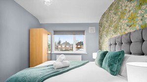 Ein modernes Schlafzimmer mit einem großen Bett, einem Holzschrank, einem Fenster mit Blick auf Häuser und einer Wand mit Muster.