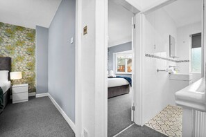 Une chambre d’hôtel comprenant un lit, une table de chevet, une lampe et une salle de bain avec un lavabo et un miroir.