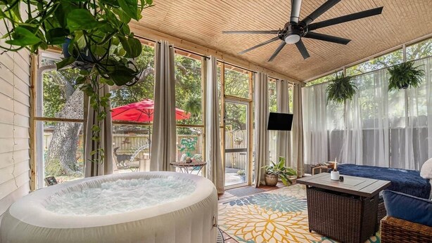 A hot tub in a covered outdoor area with a ceiling fan, wicker furniture, and a patterned rug. - Birdhouse: Pet friendly 2 Bed With Yard & Hot Tub (Charleston)