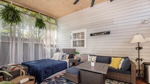 A room with a bed, a sofa, a table, wicker furniture, a patterned rug, and a window with curtains. - Birdhouse: Pet friendly 2 Bed With Yard & Hot Tub (Charleston)
