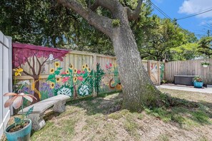 Ein Garten mit Holzpforte, Baum, Bank und Topfpflanze.