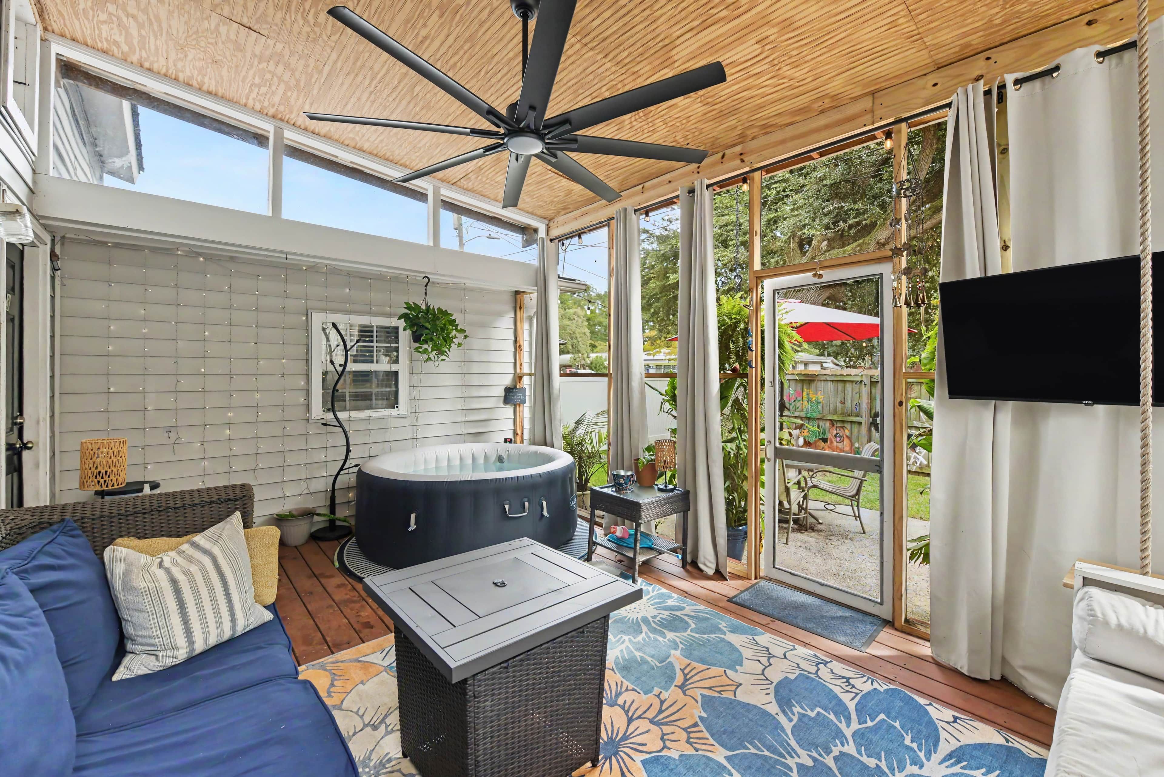Une véranda avec un ventilateur de plafond, un jacuzzi, un canapé et un téléviseur fixé au mur.