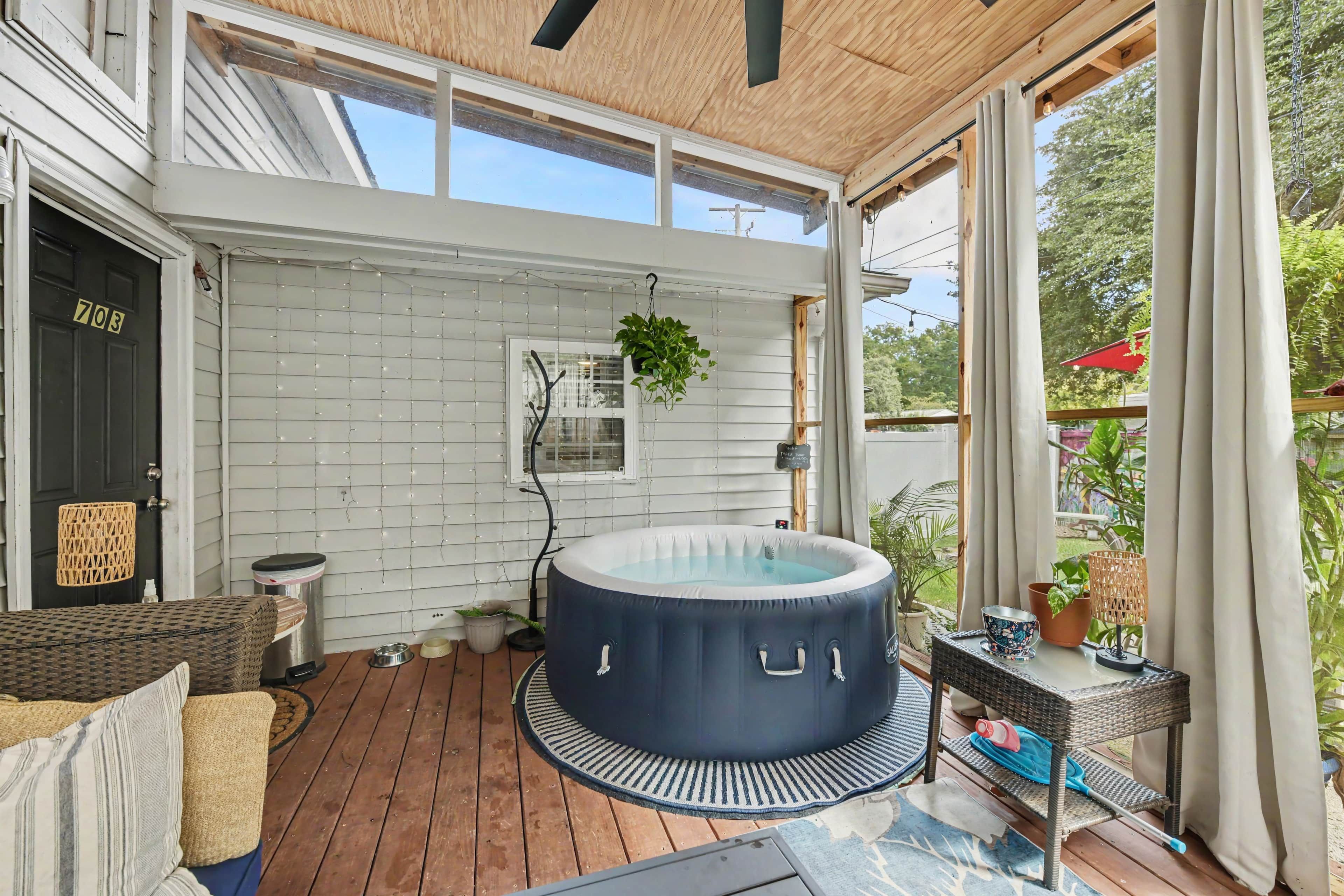 Une terrasse ensoleillée avec un jacuzzi, un canapé en osier et une vue sur un paysage verdoyant.