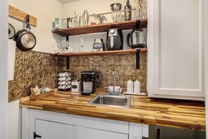 Una cocina con mostradores de madera, un lavamanos de acero inoxidable y varios electrodomésticos y utensilios en estantes.