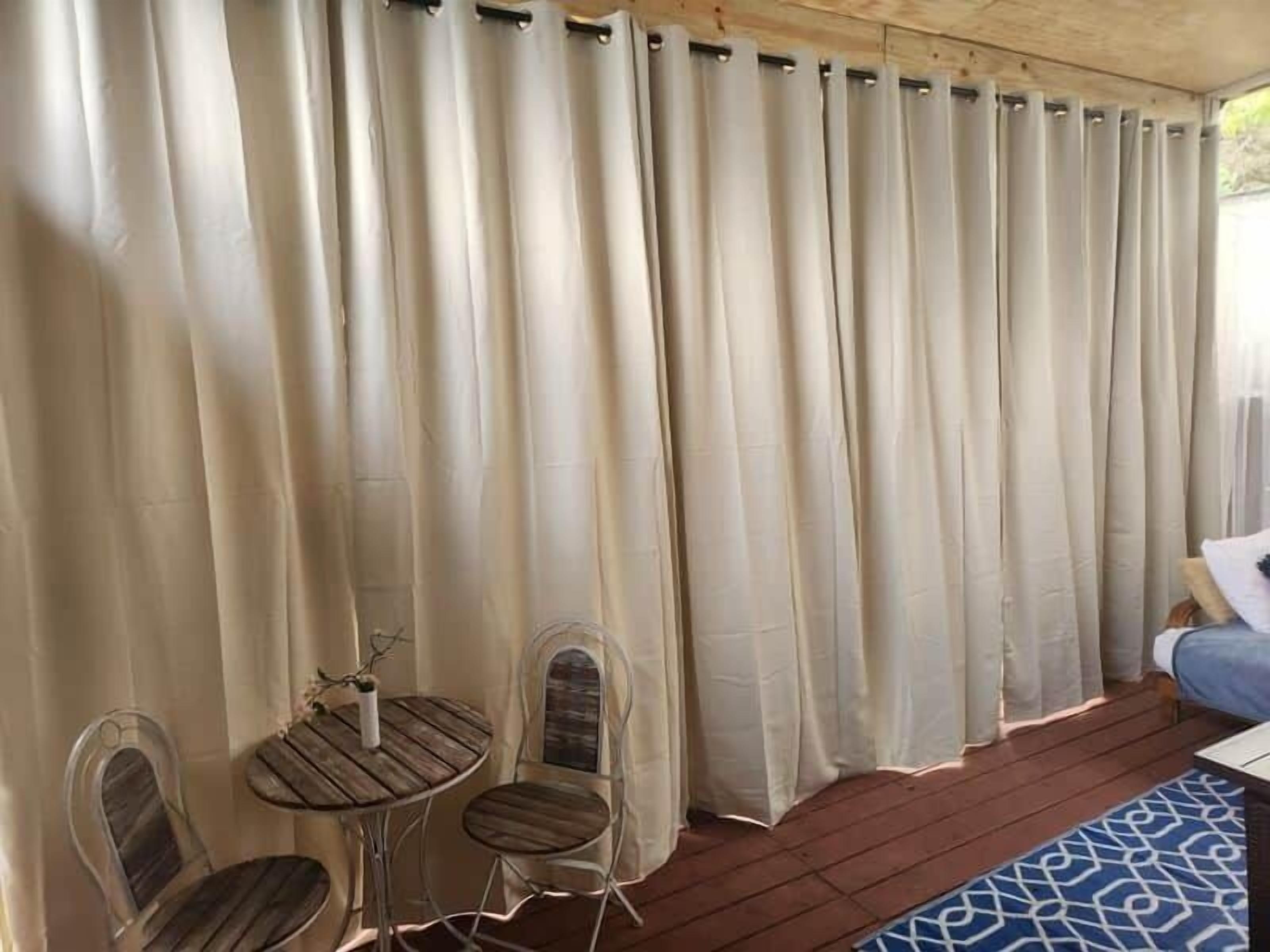 A room with a wooden ceiling, a bed, a small round table with two chairs, and a window with curtains.