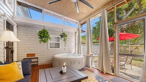 A sunroom with a hot tub, a sofa, and a table with a candle. - Birdhouse: Pet friendly 2 Bed With Yard & Hot Tub (Charleston)