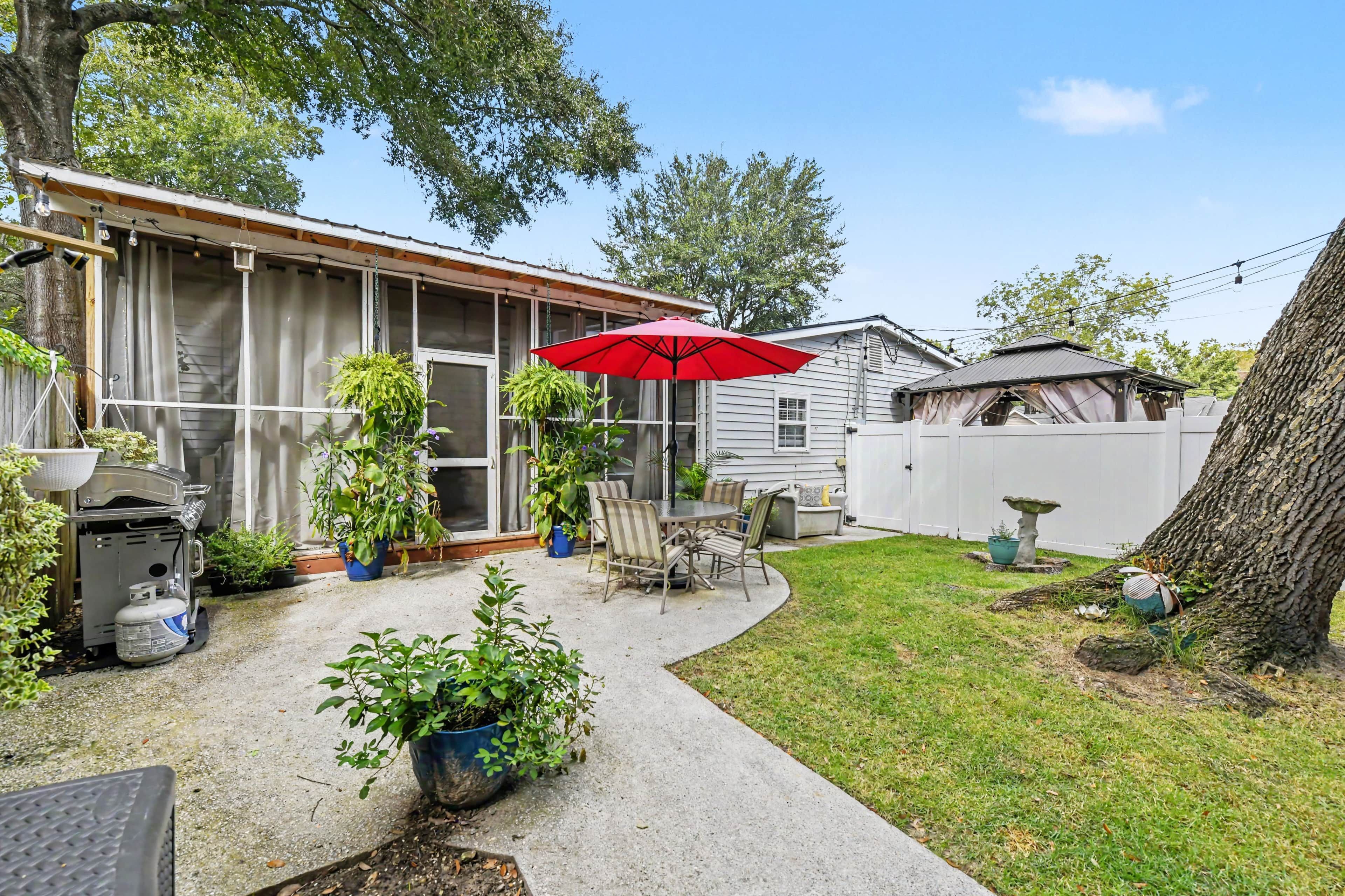 Un jardin avec une terrasse, des plantes en pot, un parasol rouge et un barbecue.