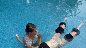 A person floating in a clear blue pool with another person standing beside them. - Birdhouse: Pet friendly 2 Bed With Yard & Hot Tub (Charleston)
