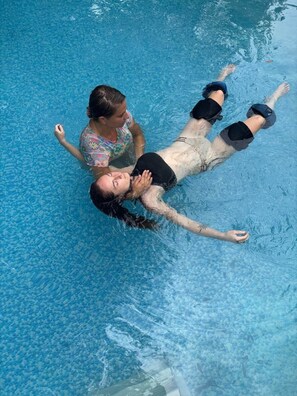 Una persona flota en una piscina azul cristalina mientras otra persona permanece de pie a su lado.
