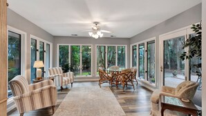 A spacious room with large windows, a ceiling fan, and a dining area with wicker chairs. - Easy Beach Living – Single-Story Coastal Retreat - 5-Minute Walk to the Beach (Hilton Head Island)