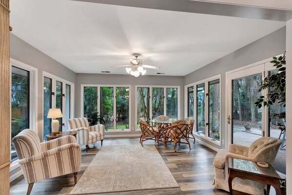 A spacious room with large windows, a ceiling fan, and a dining area with wicker chairs.