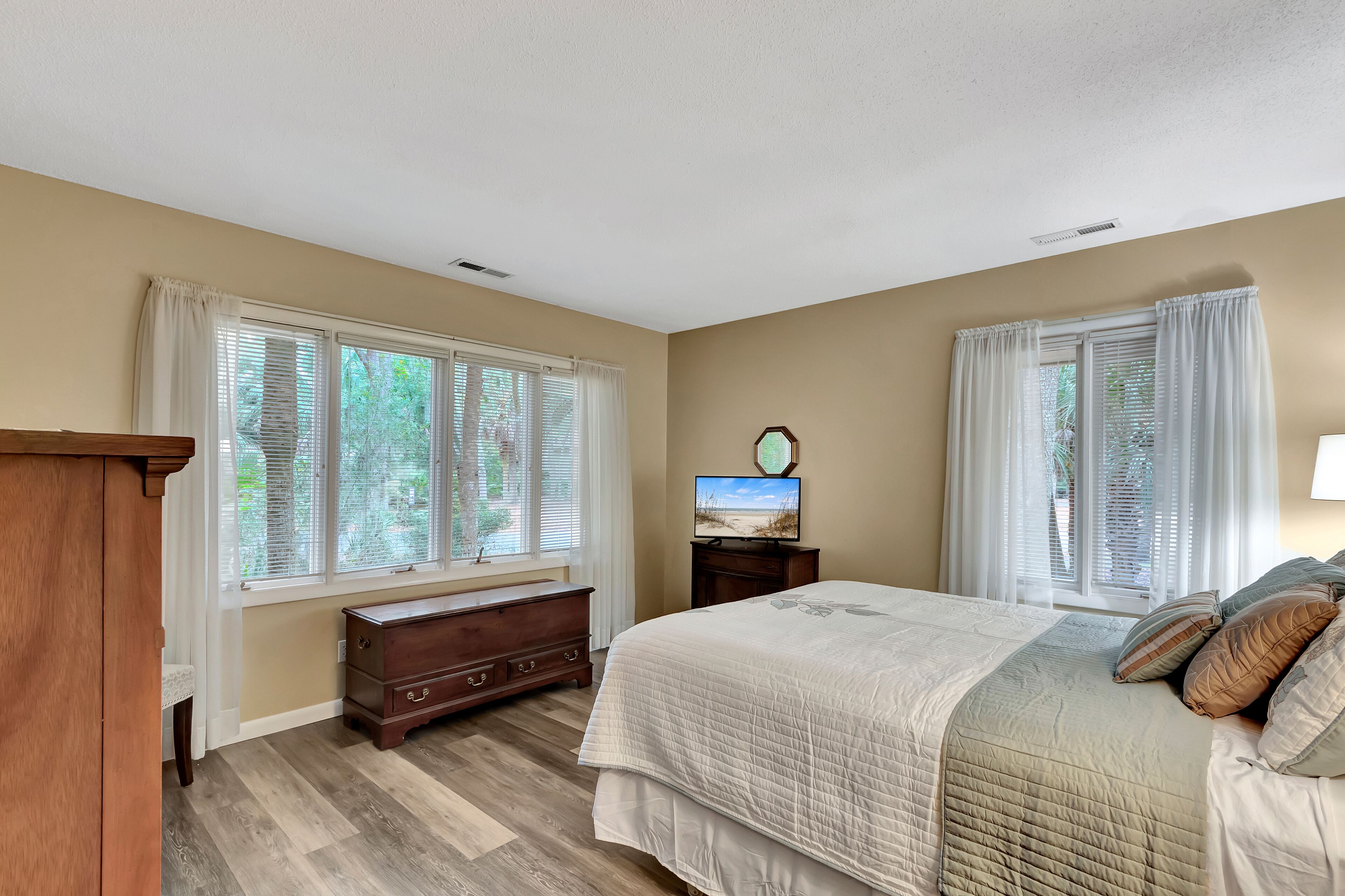 A bedroom with a large bed, a dresser, a television on a stand, and a window with blinds.