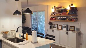 Una cocina moderna con una isla central, iluminación colgante y un estante para juegos.