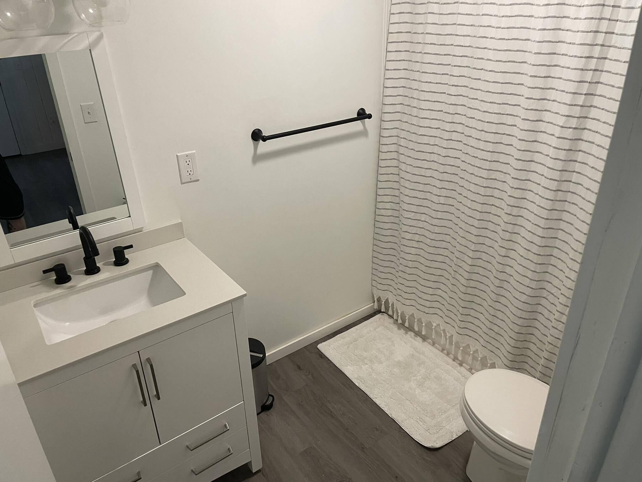 Ein Badezimmer mit Waschbecken, Spiegel und Schrank, einem Handtuchhalter, einem gestreiften Duschvorhang und einer Toilette.
