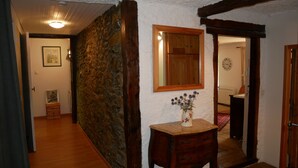 A hallway with a stone wall, wooden floor, a wooden door, a mirror, and a vase with flowers on a small table. - Exceptional and spacious apartment – Coup de Cœur – in the heart of the resort (Vars)