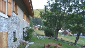 A stone building with wooden shutters, a wooden table and chairs in the yard, and a view of houses in the background. - Exceptional and spacious apartment – Coup de Cœur – in the heart of the resort (Vars)