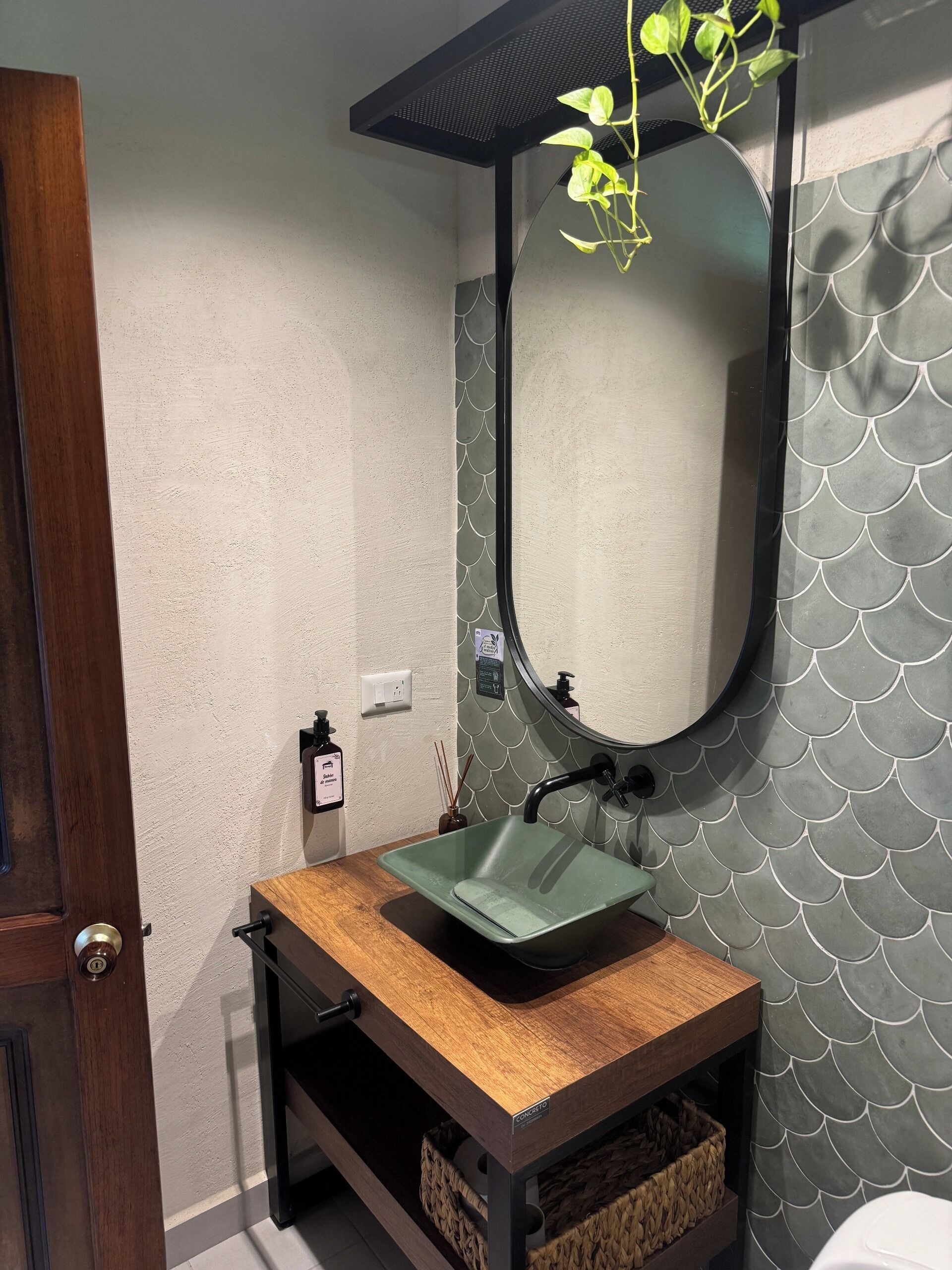 Un baño con tocador de madera, lavamanos verde y espejo con borde festoneado.