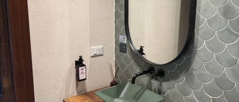A bathroom with a wooden vanity, a green sink, and a mirror with a scalloped edge.