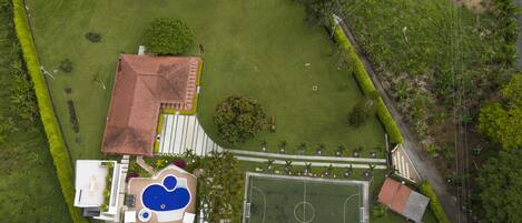 An aerial view of a property with a swimming pool, tennis court, and a building with a red roof.