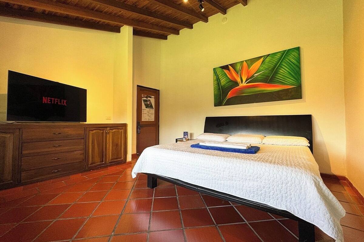 Ein Schlafzimmer mit Bett, Fernseher, einem Gemälde und einem Holzkasten.