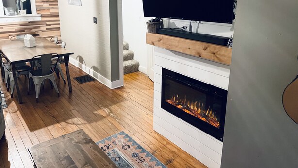 Un salon moderne doté d’une cheminée, d’un téléviseur à écran plat fixé au mur et d’un coin repas avec une table et des chaises en bois.