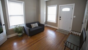 Une pièce dotée d’un parquet, d’un canapé de couleur foncée agrémenté d’un coussin à rayures, d’une plante en pot et d’un banc en métal.