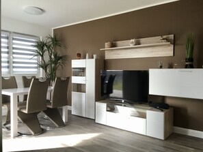 Ein modernes Wohnzimmer mit Essbereich, einem Flachbildfernseher und minimalistischem Design.
