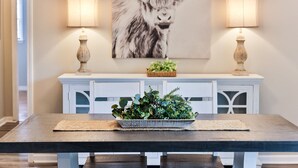 A dining area with a wooden table, a decorative plant centerpiece, and a wall-mounted painting of a yak.