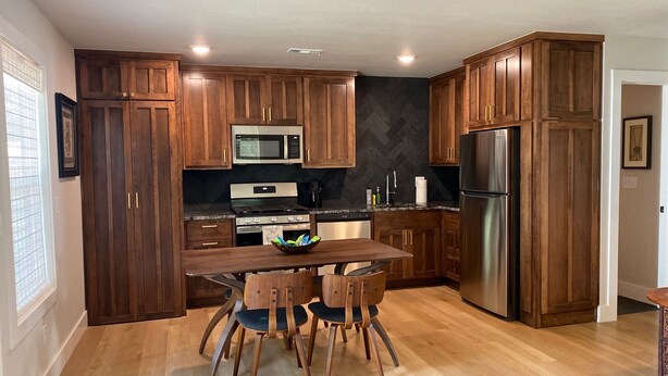 Une cuisine moderne avec des meubles en bois, des appareils électroménagers en acier inoxydable et un coin repas doté de chaises en bois.